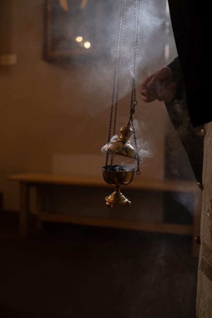 A close-up of an orthodox censer with smoke rising in a dimly lit indoor setting.