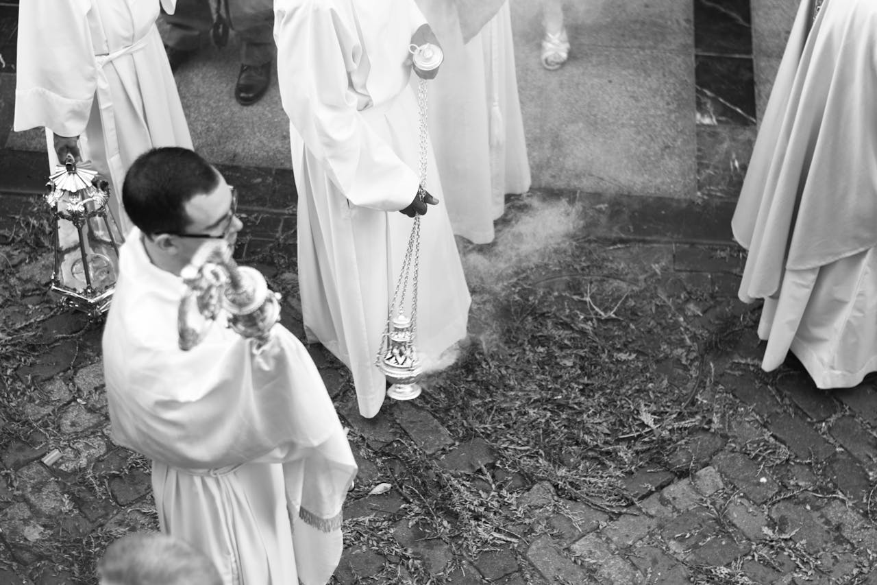 Black and white photo of a religious procession with priests carrying incense outdoors.
