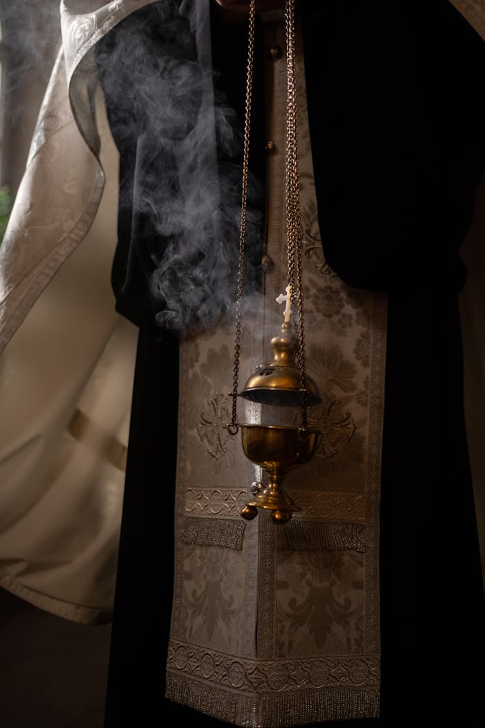 Orthodox priest holding a censer with smoke indoors, evocative of religious rituals.